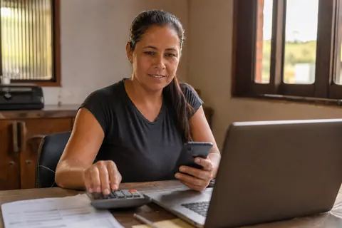 Sócia de uma empresa de perfuração de poços conferindo as contas da empresa no notebook e no celular