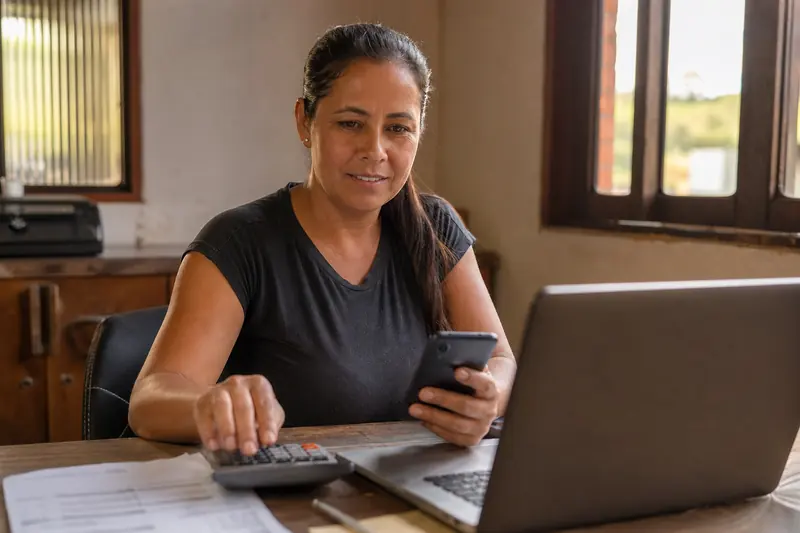Sócia de uma empresa de perfuração de poços conferindo as contas da empresa no notebook e no celular